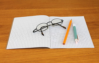 Open graph paper notebook with glasses, pencil, and pen on wooden desk