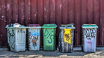 Row of graffiti-covered waste bins against a red corrugated metal wall