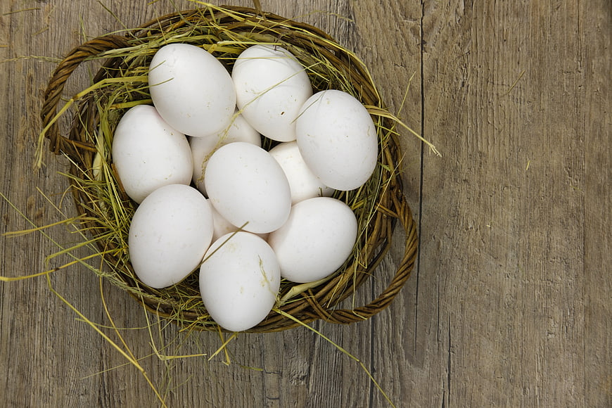 White Eggs In Wicker Basket On Rustic Wood