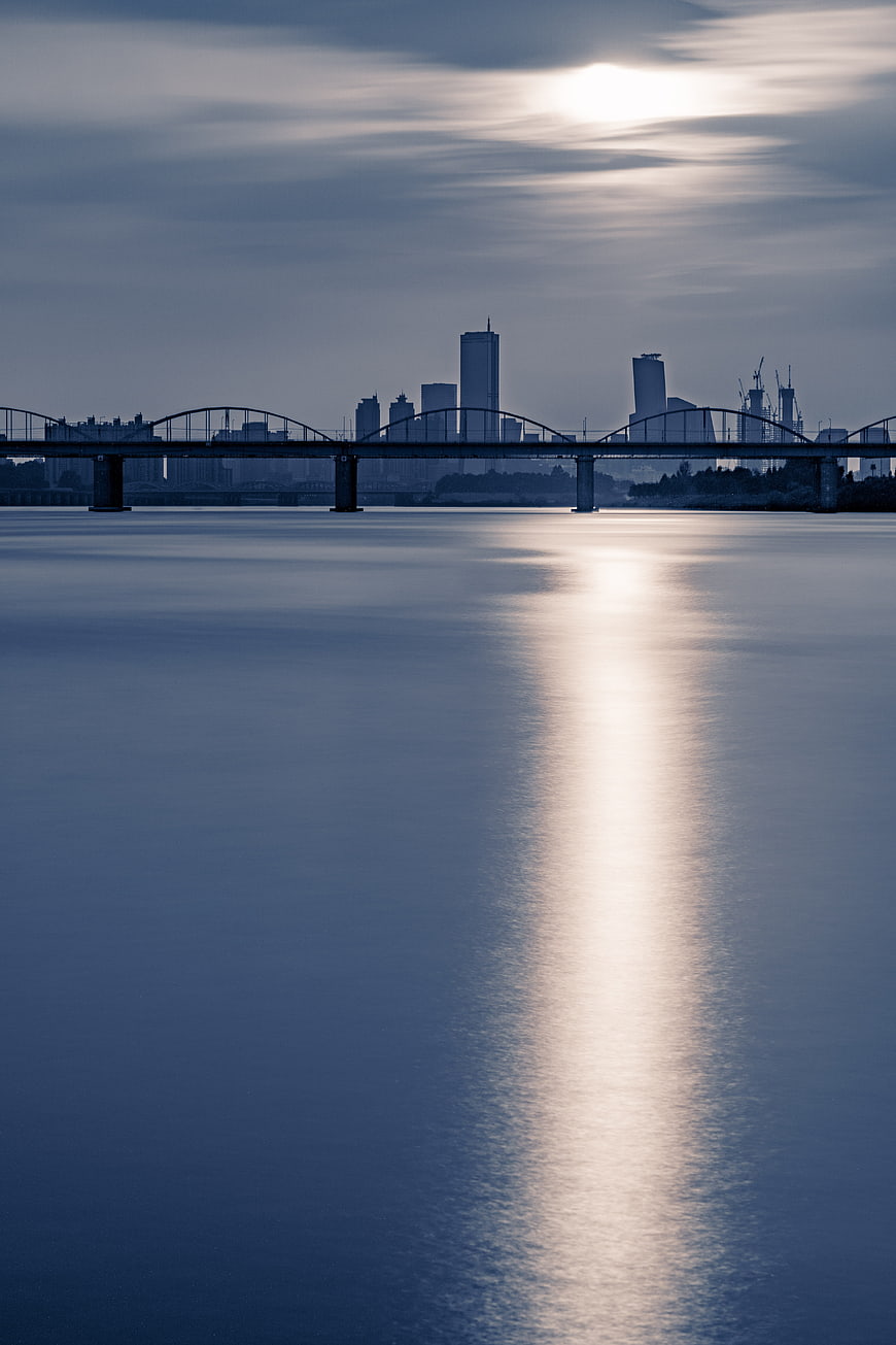 City skyline and bridge silhouette with sun reflection on calm river water