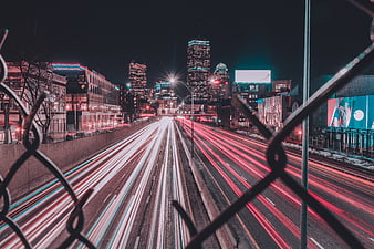 Night city traffic light trails through chain link fence