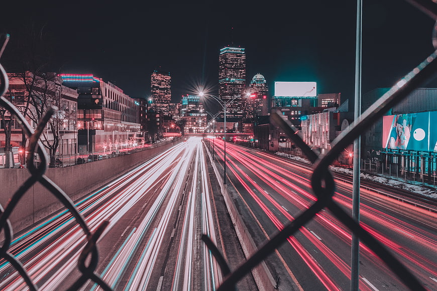 Night city traffic light trails through chain link fence