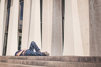 Man lying on steps in front of modern building pillars