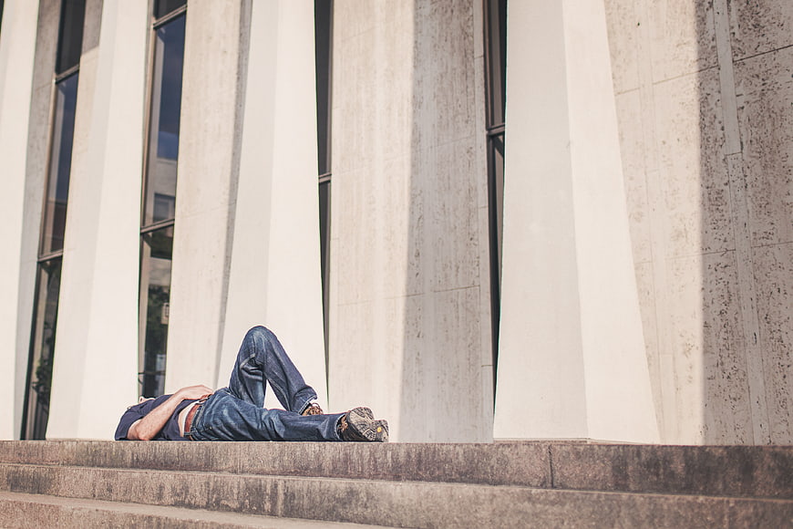 Man lying on steps in front of modern building pillars