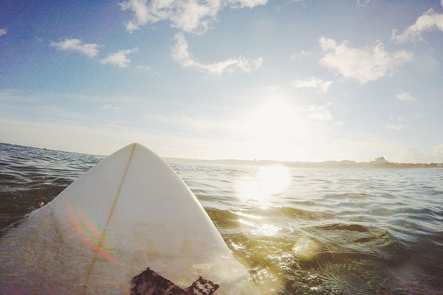 Surfboard Nose in Ocean Water with Blue Sky and Sun