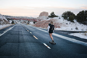 Woman Skateboarding on Desert Highway at Sunset