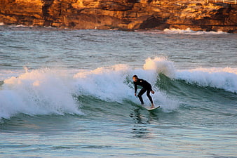 Surfer Riding Wave at Sunset Near Rocky Cliffs