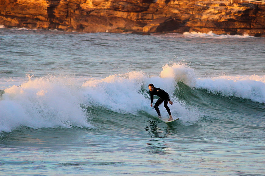 Surfer Riding Wave at Sunset Near Rocky Cliffs