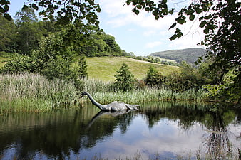 Nessie statue in a calm Scottish loch with green hills and trees