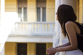 Woman leaning on balcony railing looking at yellow building