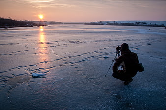 Photographer capturing sunset on frozen lake in winter