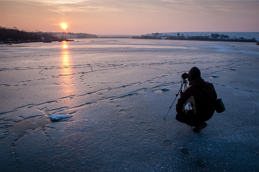 Photographer capturing sunset on frozen lake in winter
