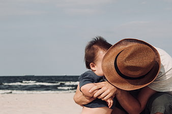 Father holding toddler son on sandy beach with ocean background