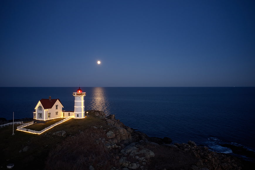 Lighthouse on Rocky Coast at Night with Moon