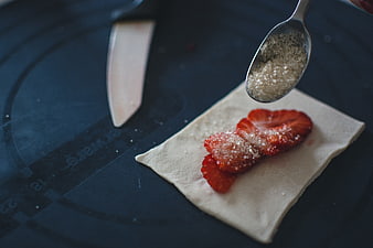 Sprinkling sugar on strawberry pastry dough close-up
