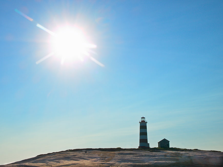 Red and White Striped Lighthouse on Rocky Coastline Under Bright Sun