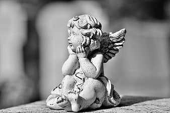 Black and white close-up of a weathered stone cherub statue