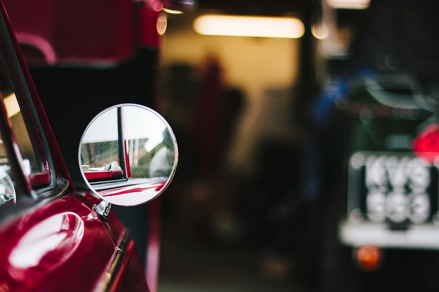 Close-up of red car side mirror with blurred garage background