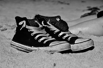 Black high-top sneakers on sandy beach with blurred legs