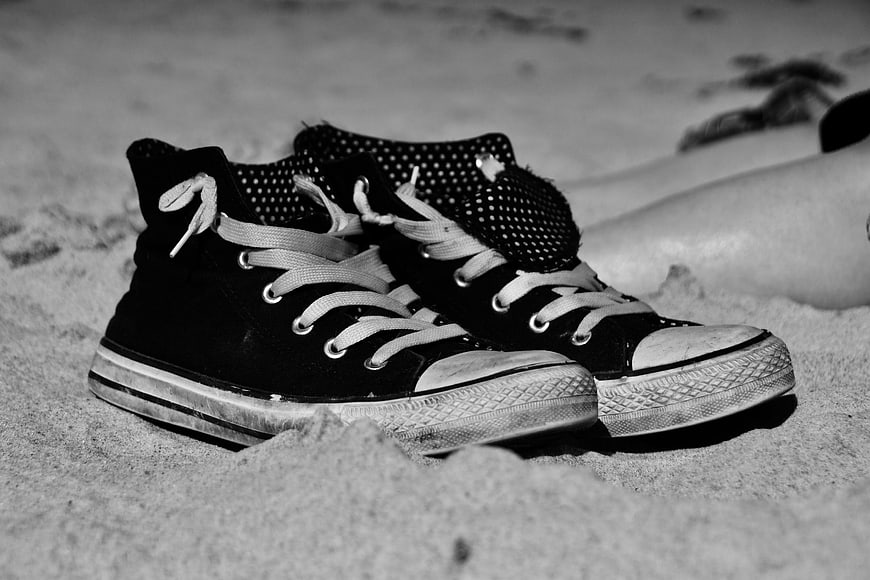 Black high-top sneakers on sandy beach with blurred legs