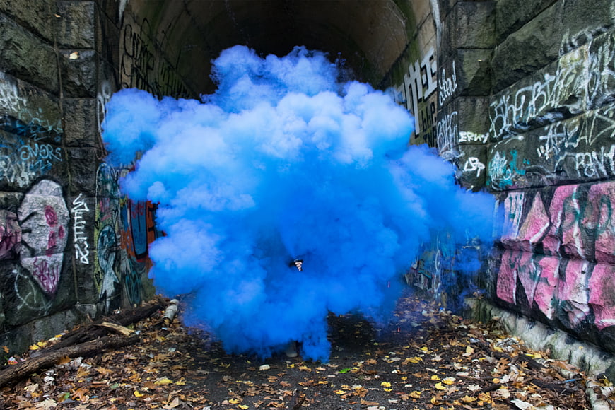 Blue smoke bomb in graffiti tunnel with autumn leaves