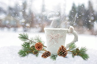 Steaming white mug with pine branches and cones in snow