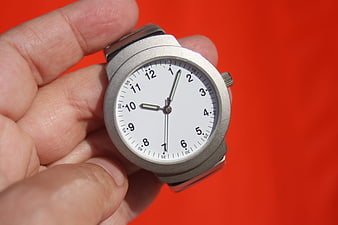 Silver wristwatch held in hand against red background