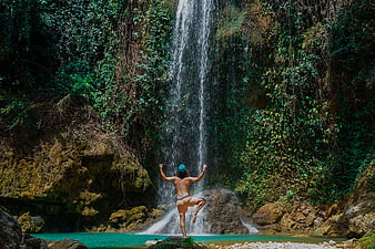 Man meditating in yoga pose under tropical waterfall