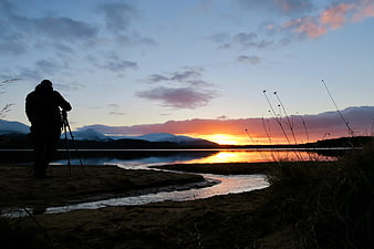 Silhouette of photographer capturing sunset over lake and mountains