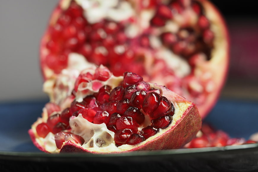 Close-up of fresh pomegranate seeds and fruit halves on a dark plate