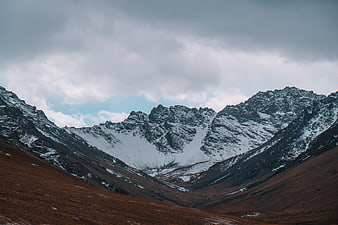 Snowy mountain peaks with brown valley and cloudy sky