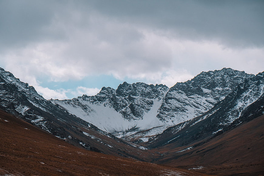 Snowy mountain peaks with brown valley and cloudy sky