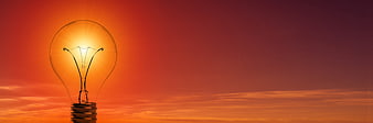 Glowing lightbulb against vibrant orange sunset sky background