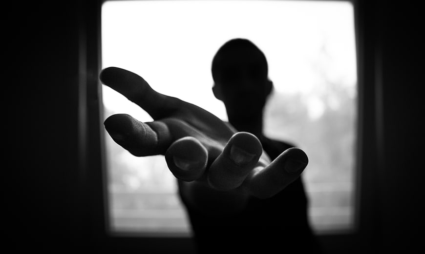 Silhouette of hand reaching through window frame