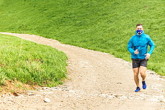 Male runner wearing blue anti-smog mask on green trail