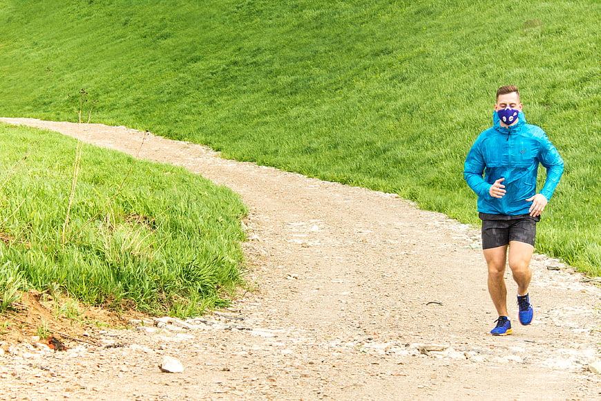 Male runner wearing blue anti-smog mask on green trail
