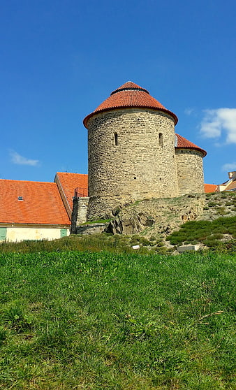 Historic stone rotunda tower with red roof on grassy hill