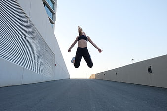 Woman jumping in black activewear on urban rooftop