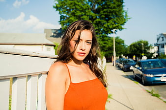 Young Woman in Orange Top Leaning on White Fence Outdoors