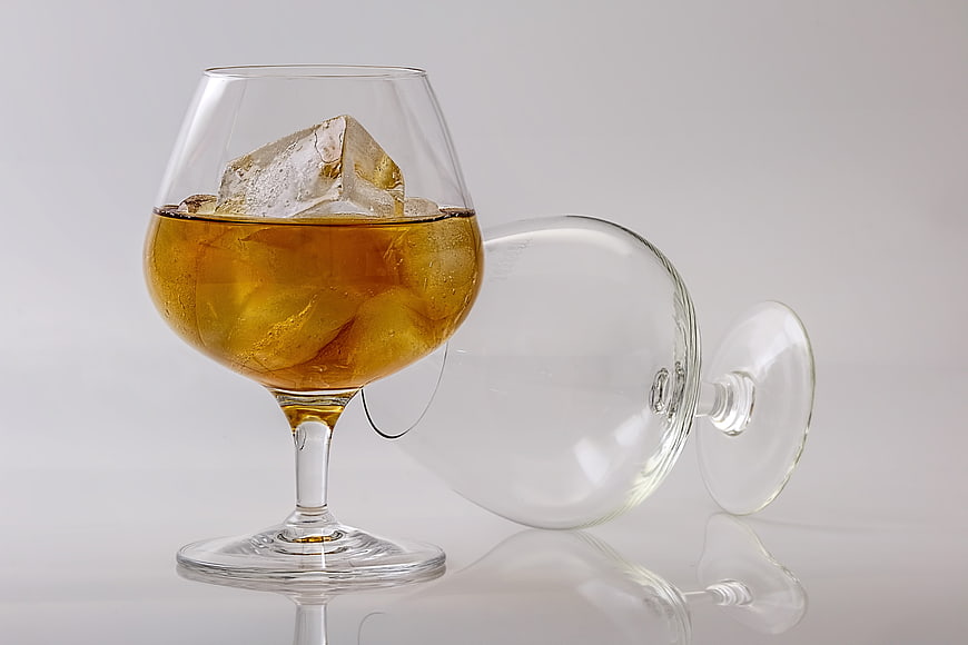 Glass of amber whiskey with ice and empty glass on white background