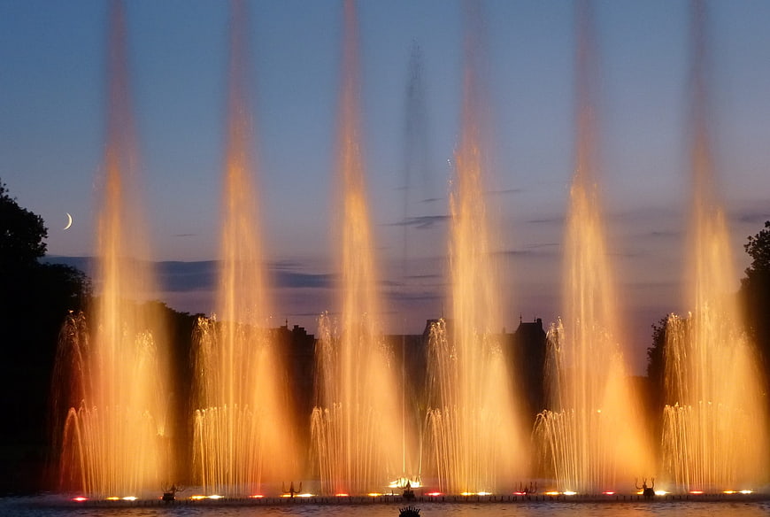 Illuminated water fountain jets at dusk with crescent moon