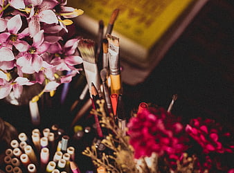 Artistic still life with pink flowers, paintbrushes, and colored pencils