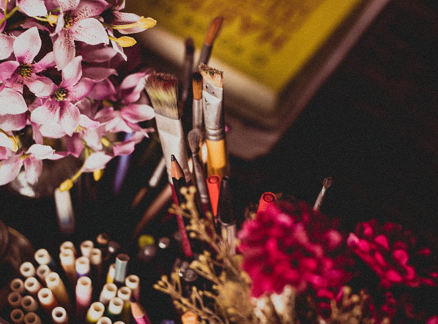 Artistic still life with pink flowers, paintbrushes, and colored pencils