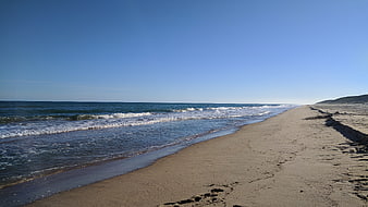 Serene sandy beach with gentle waves and clear blue sky