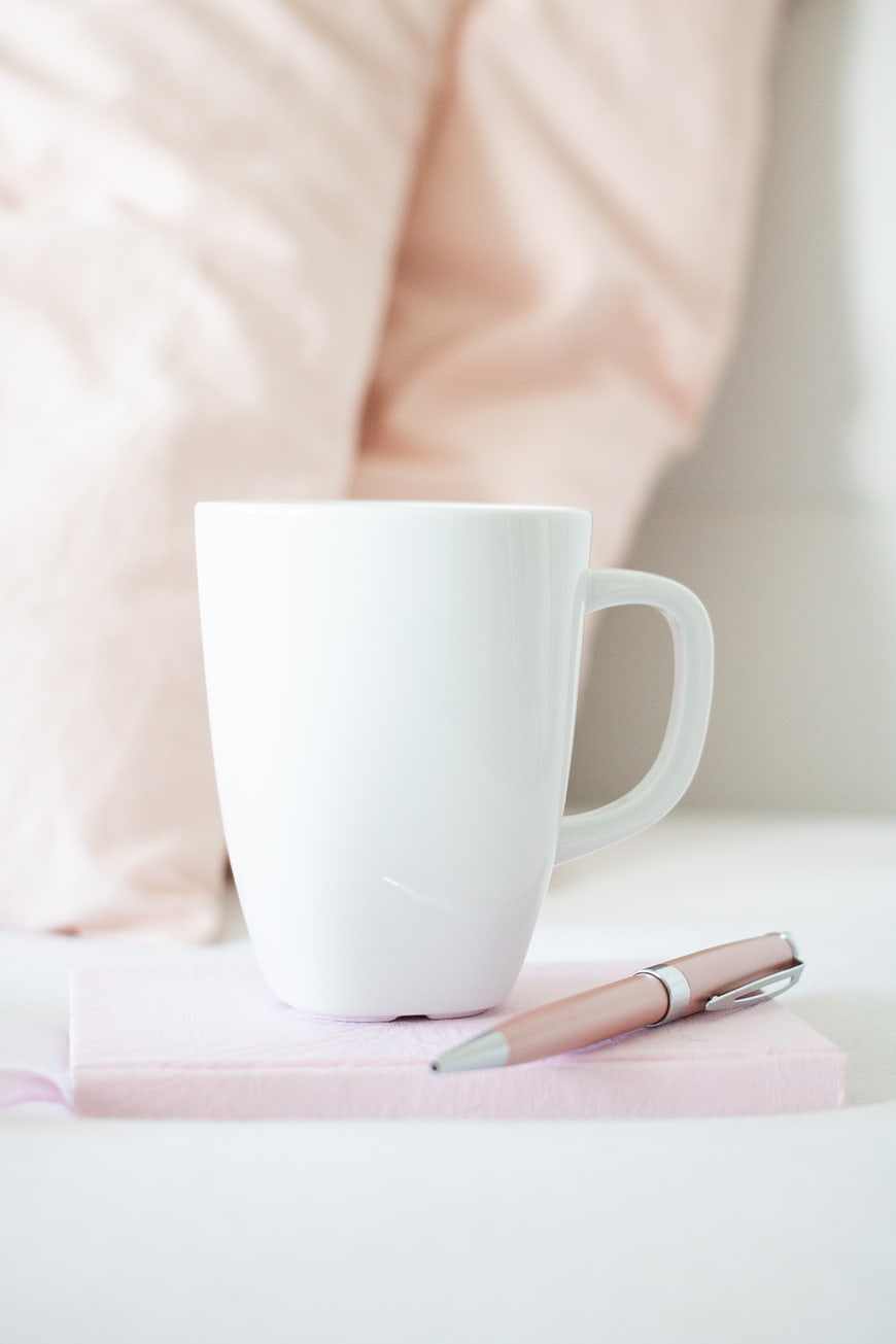 White Mug and Pen on Pink Notebook in Soft Light