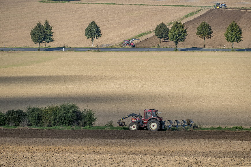 Red tractor plowing agricultural field landscape