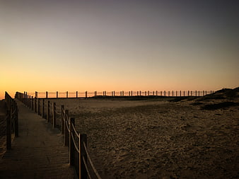 Wooden boardwalk leading to beach at sunset with rope fence