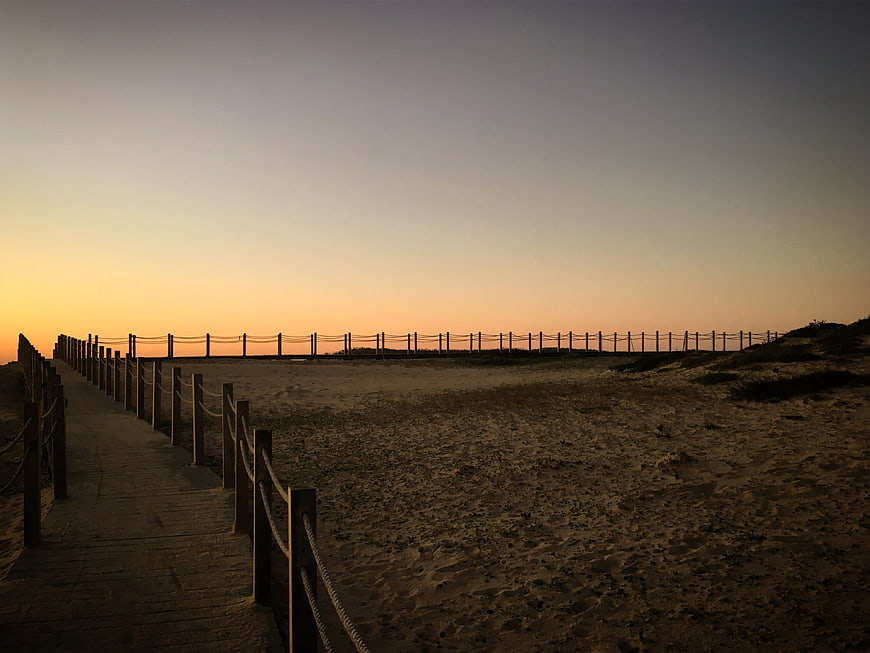 Wooden boardwalk leading to beach at sunset with rope fence