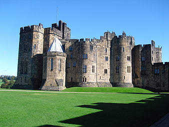 Alnwick Castle exterior with green lawn and blue sky