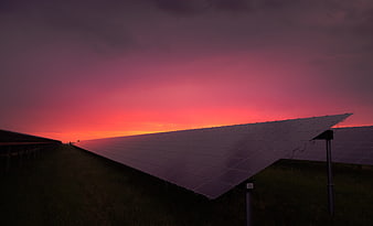 Solar panels in a field at sunset with a vibrant pink and orange sky